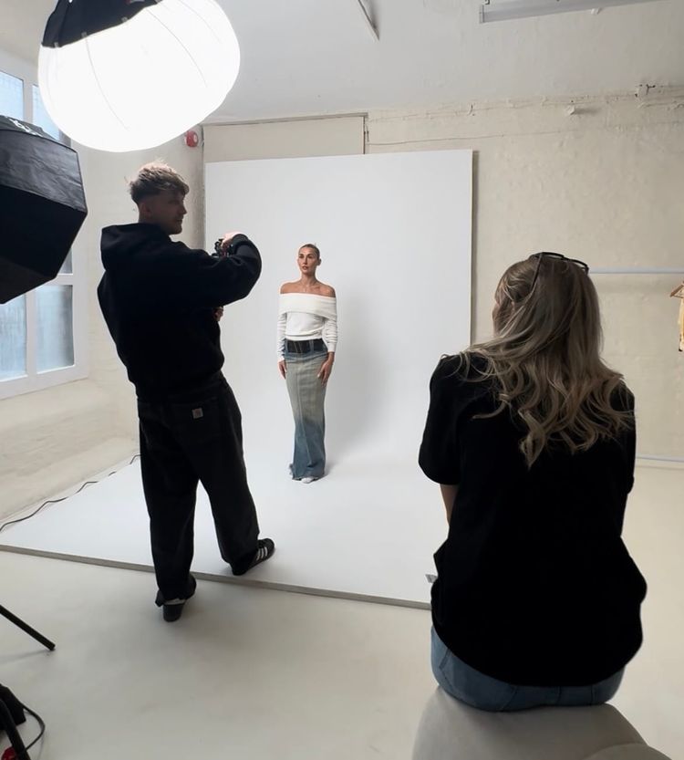 Behind-the-scenes of a fashion photoshoot with a photographer shooting a model in front of a white backdrop.