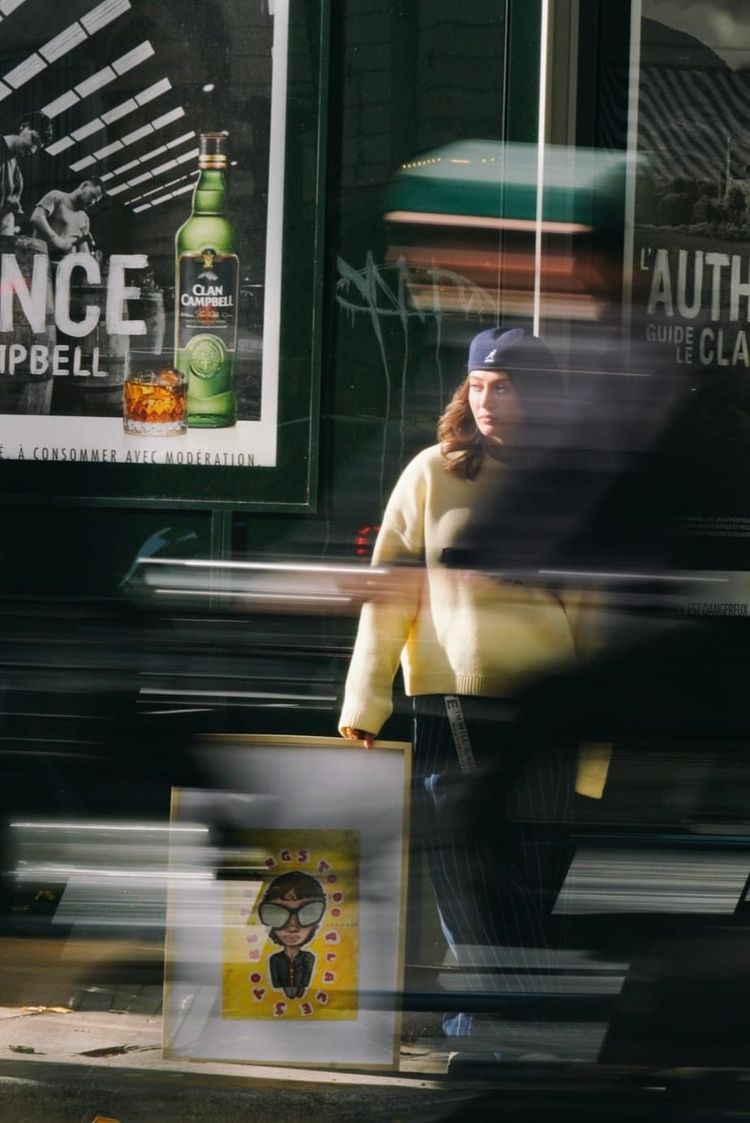 An artist holding her artwork on the other side of the street with a motion blurred bike moving through the frame