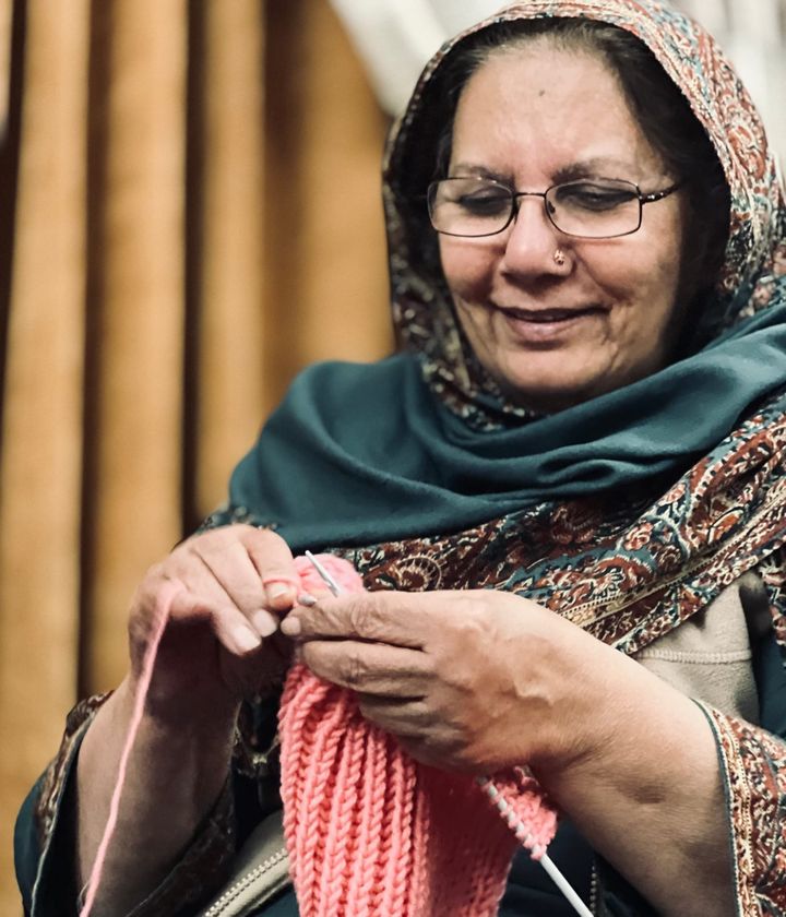 Photo of my grandma smiling and knitting me a pink woollen scarf.