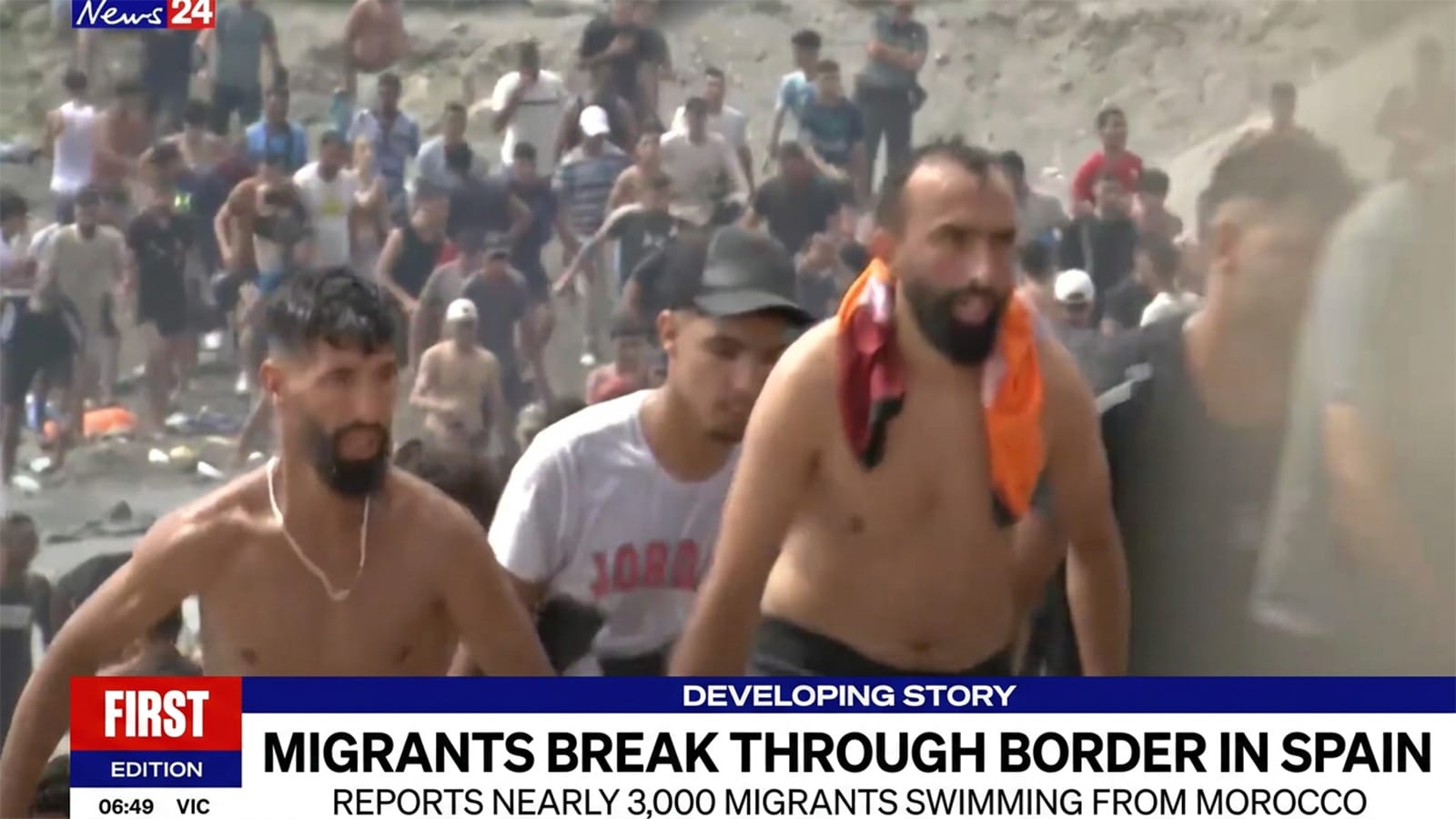 Crowd of men climbing a rocky slope into Ceuta after crossing the border.