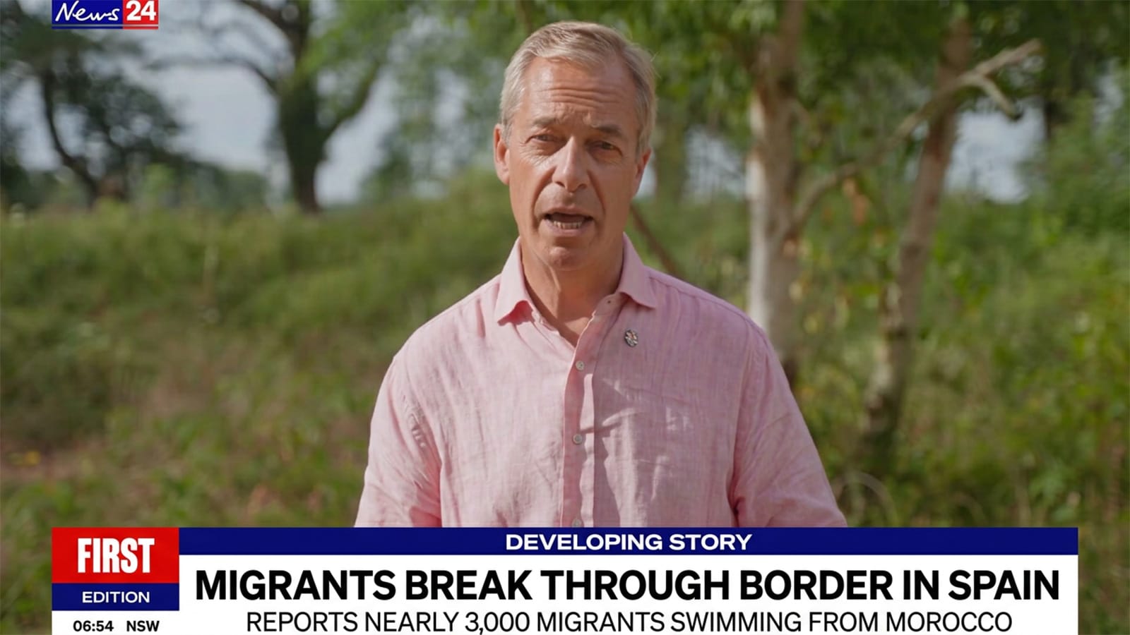 Nigel Farage speaking to camera outdoors in a pink shirt.