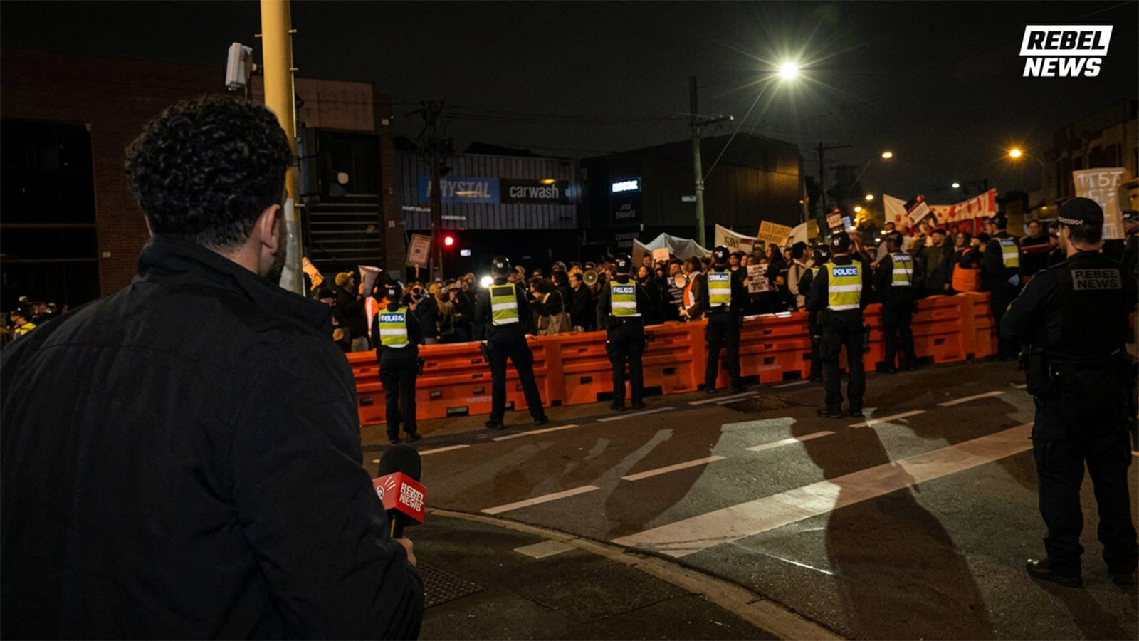 Reporter filming police officers standing behind orange barriers at night