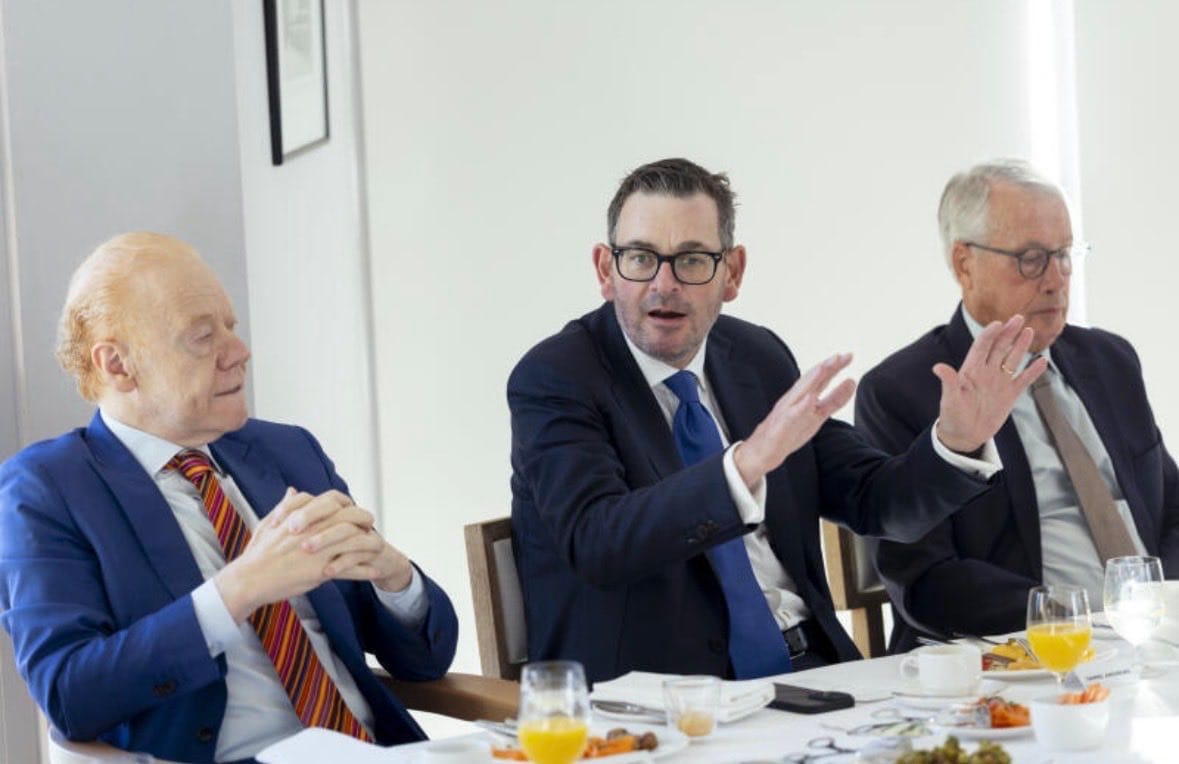 Daniel Andrews gestures while seated at a lunch table with two other men
