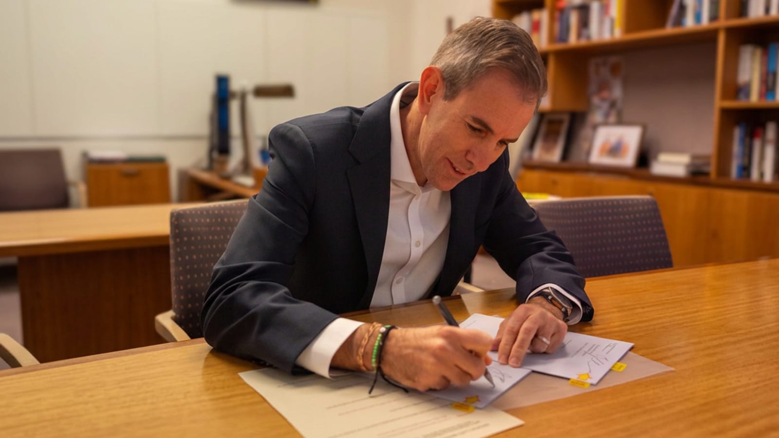 Jim Chalmers signing a document at a desk in his office