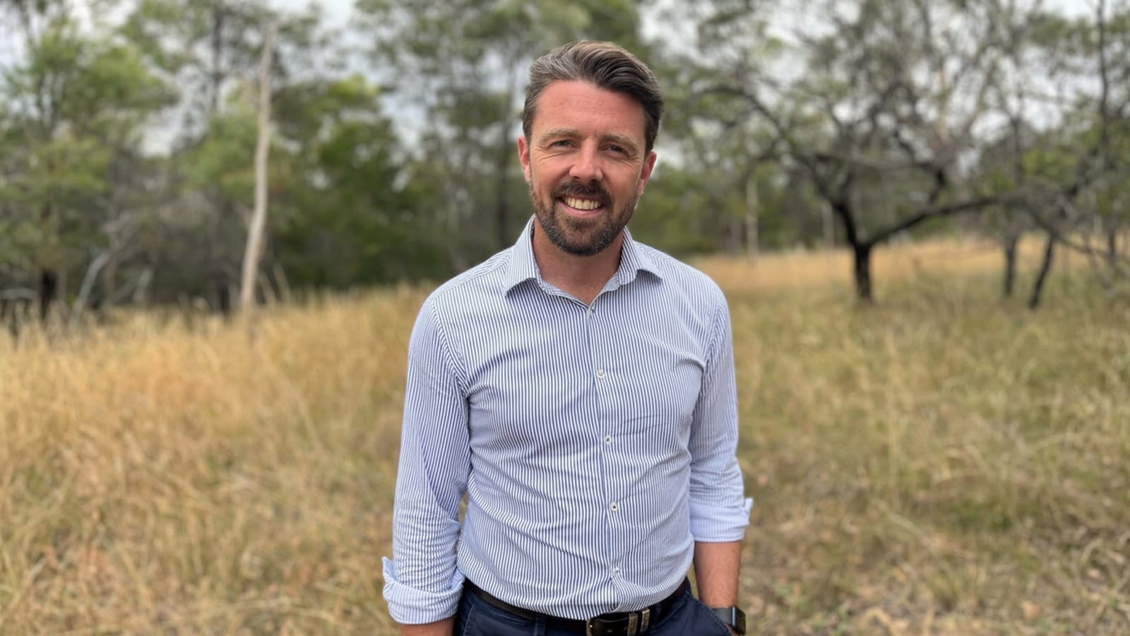Jonno Duniam standing in dry bushland wearing a striped shirt