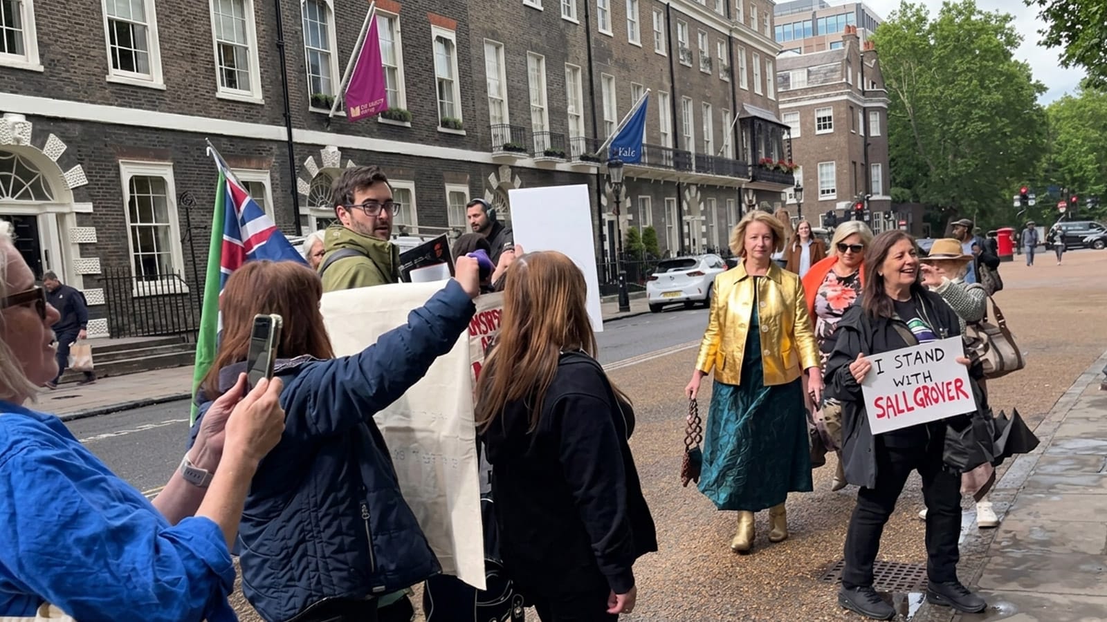 Julia Gillard walks past London protesters holding a Sall Grover sign