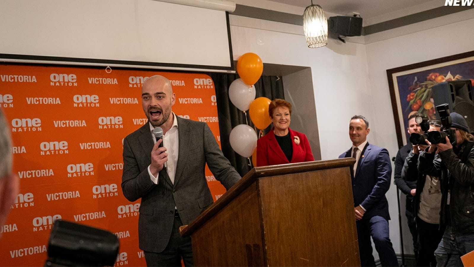 Mark Nicholson speaking at a lectern with Pauline Hanson standing behind him