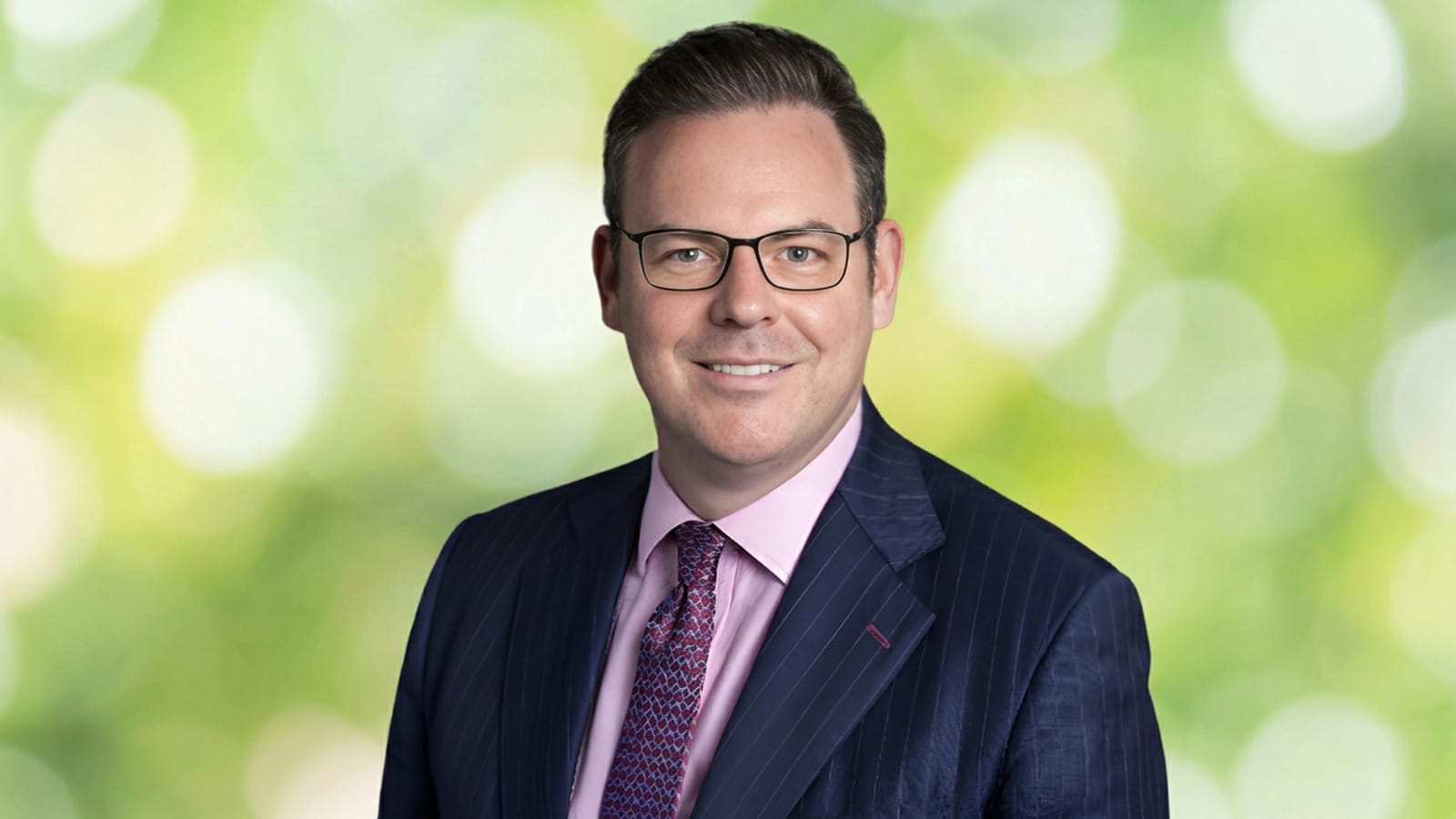 Mike Newman in a navy pinstripe suit and glasses