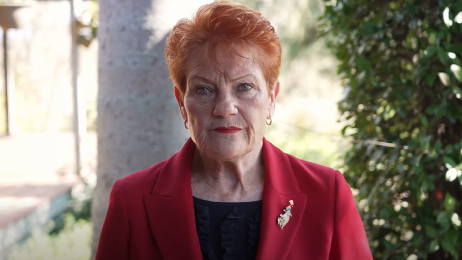 Pauline Hanson speaking outdoors in a red blazer in a One Nation video