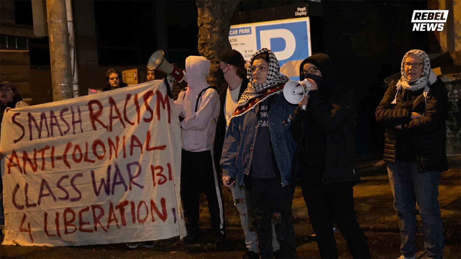 Protesters holding a large hand painted banner outside a Melbourne hotel at night
