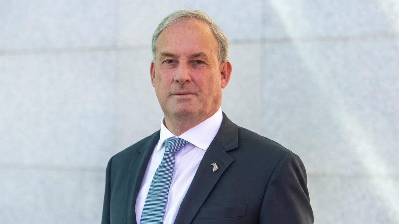 Richard Colbeck in an official portrait against a grey wall.