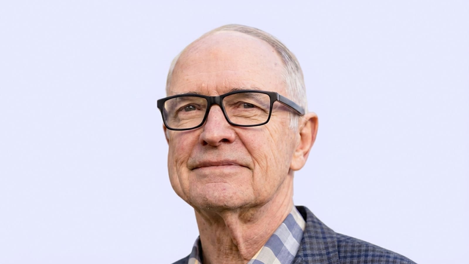 Ross Garnaut in black glasses and a checked jacket, plain background.