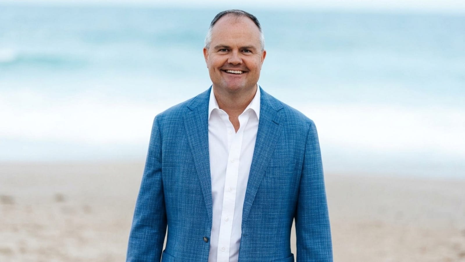 Ted O'Brien in a blue jacket standing on a beach