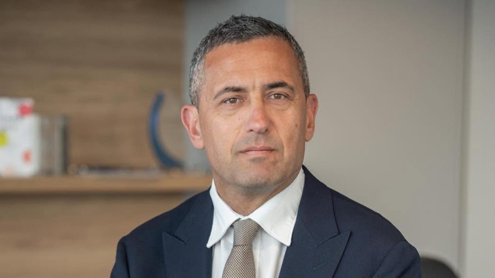 Tom Koutsantonis in a navy suit and tan tie in an office.