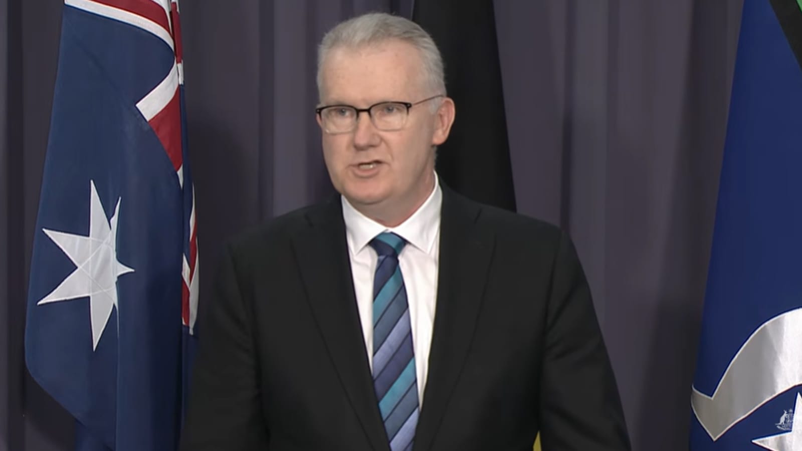 Tony Burke speaking at a Canberra press conference in front of flags