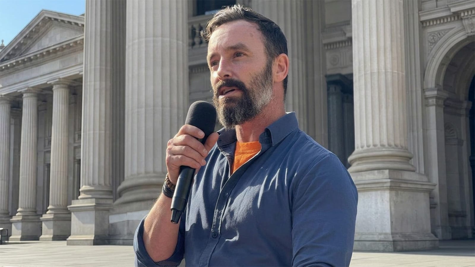 Warren Pickering speaking into a microphone outside a stone building