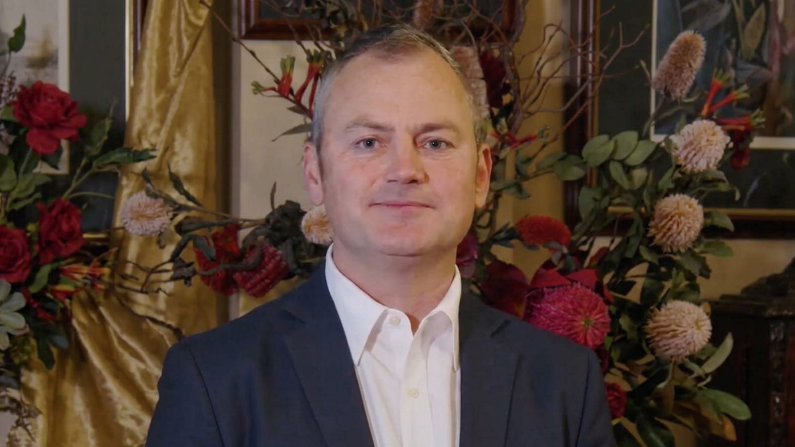 Simon Holmes à Court in a dark suit before a floral display.