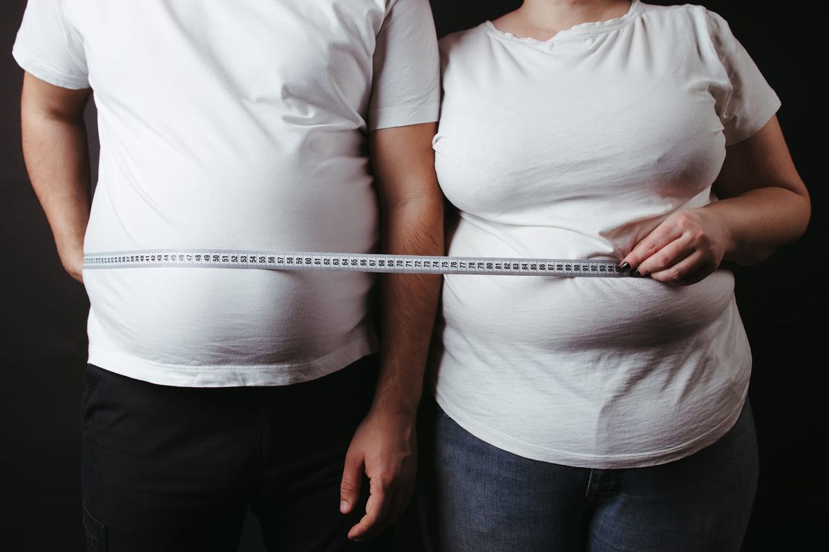 Male and female bodies with high BMI holding tape measure across their midsections