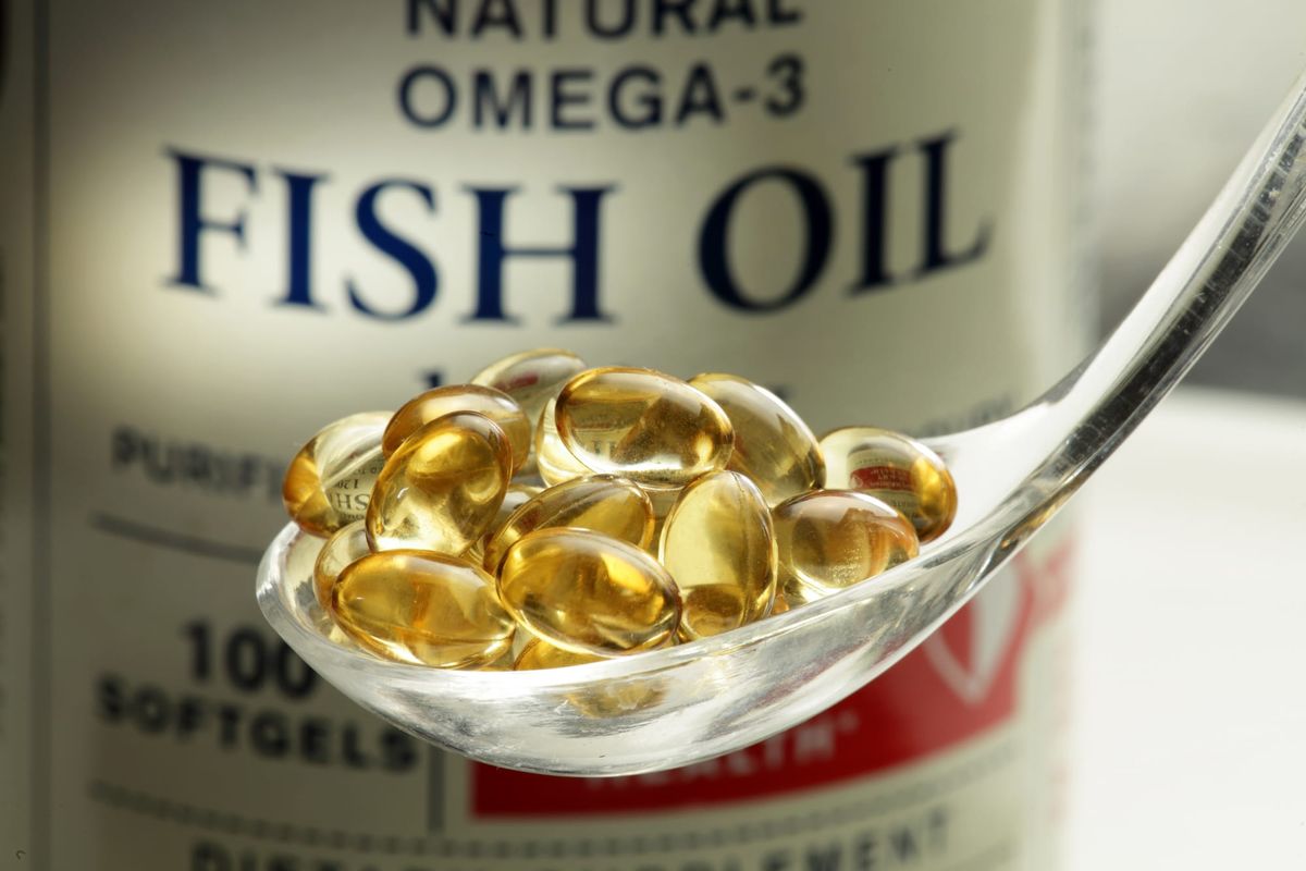A bottle of fish oil supplements behind a clear spoon of fish oil capsules