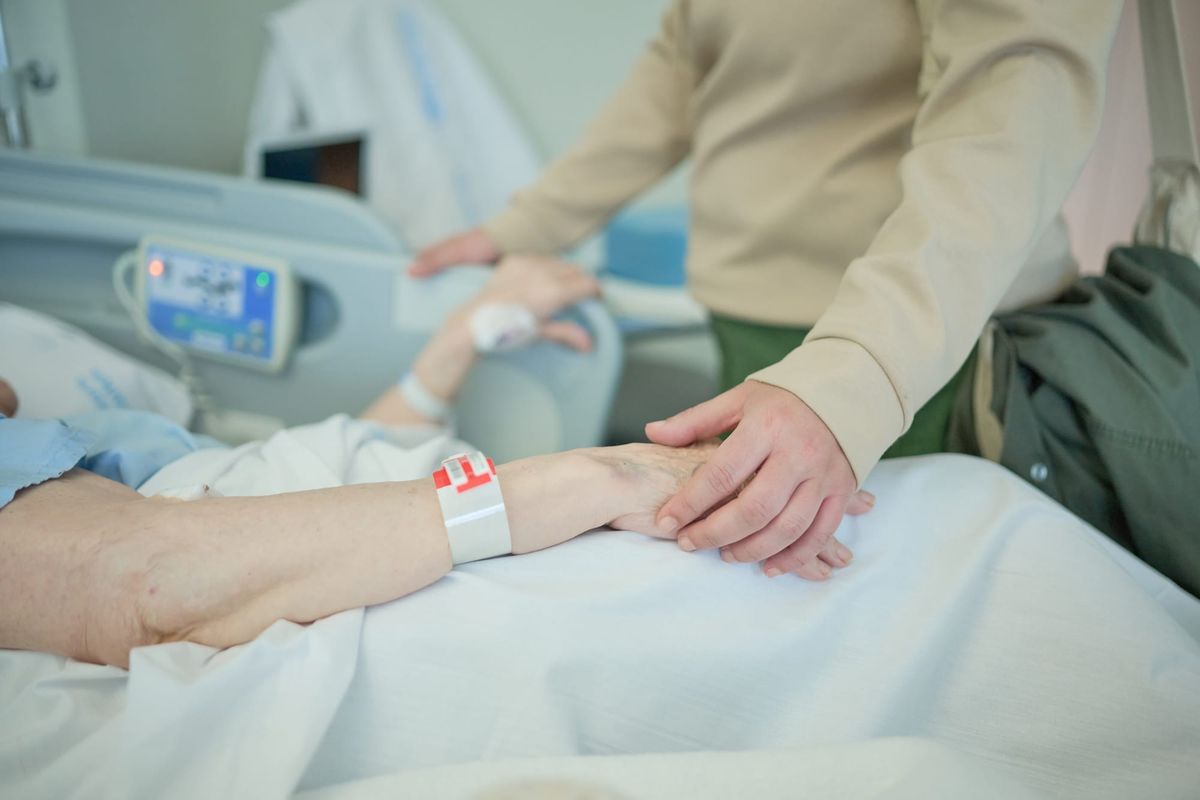Person holding hand of patient in hospital bed.