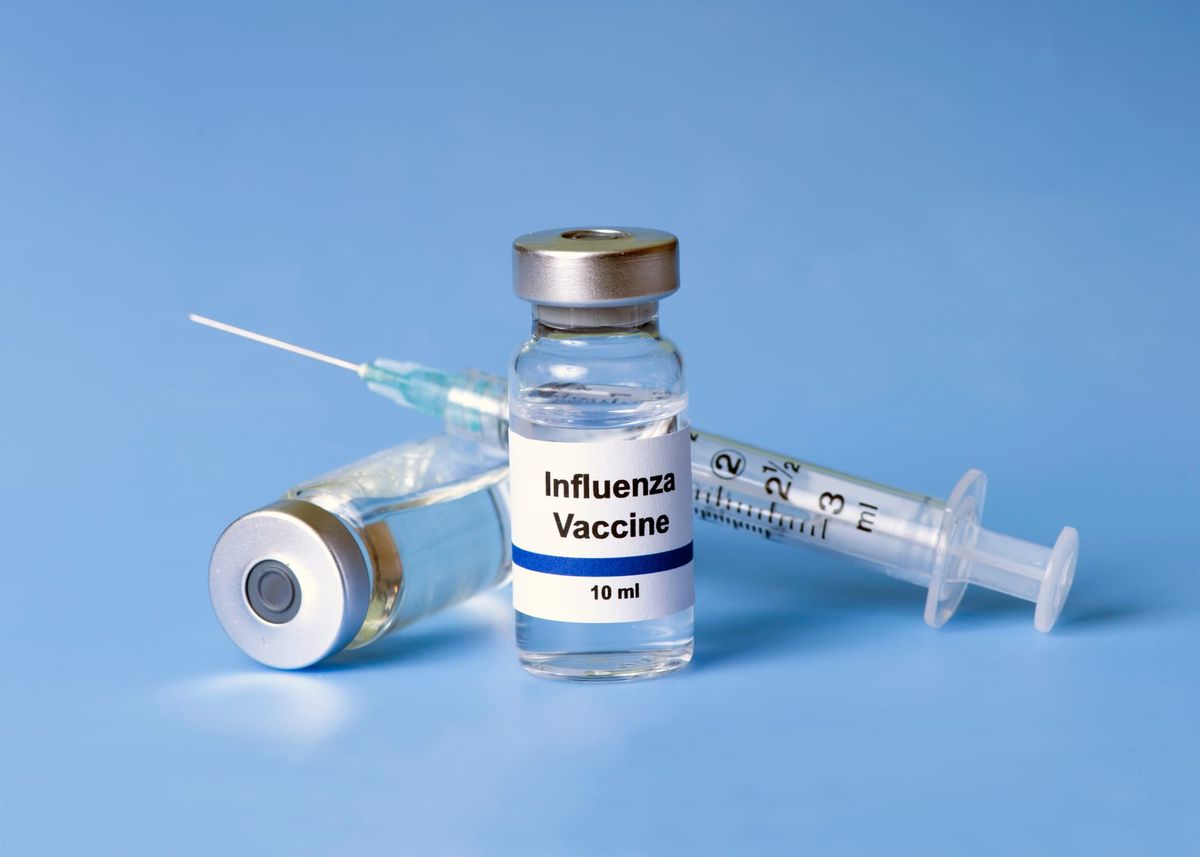 Two vials of influenza vaccine and a syringe and needle.