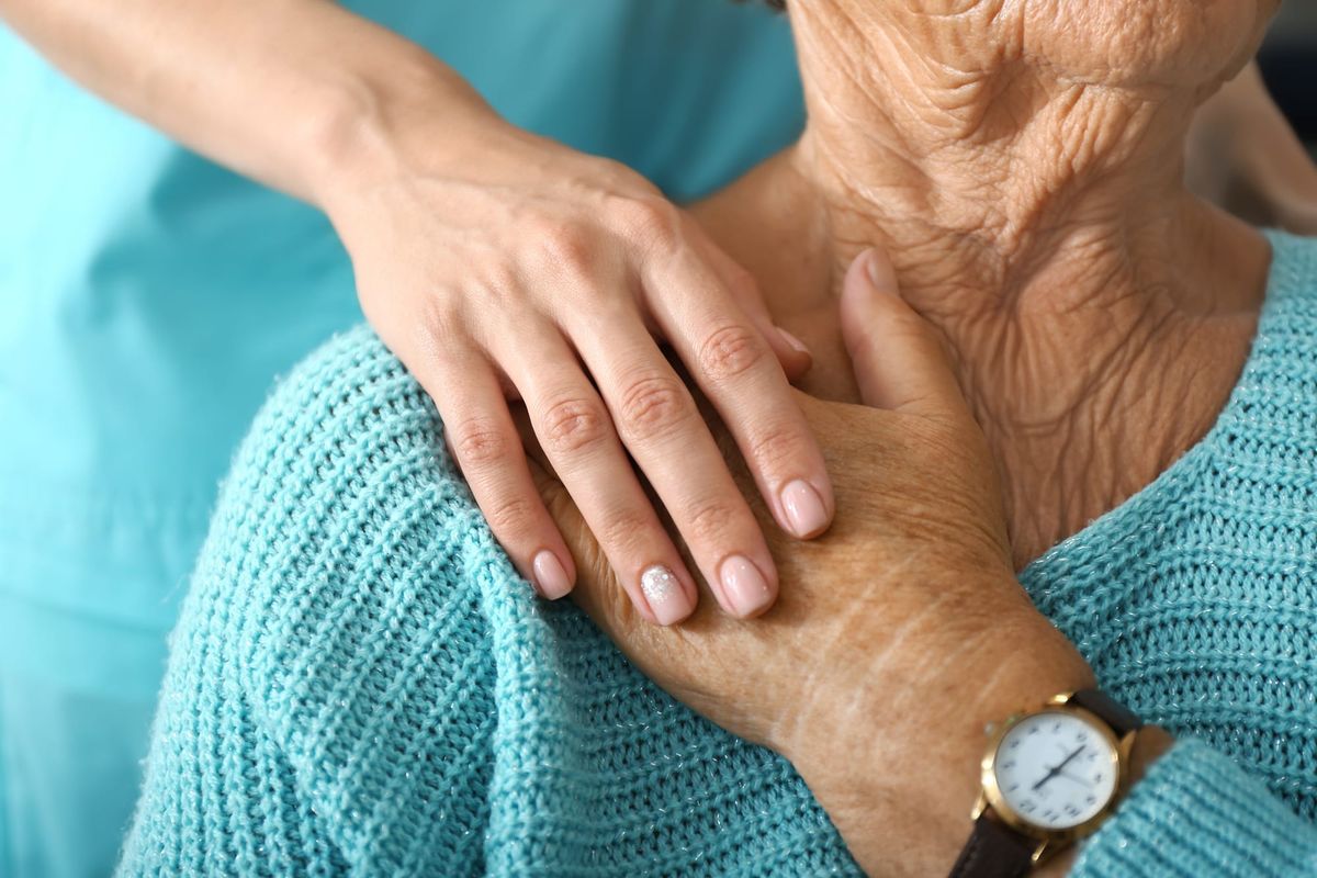 A young woman's hand rests on an older woman's hand in a comforting manner. 