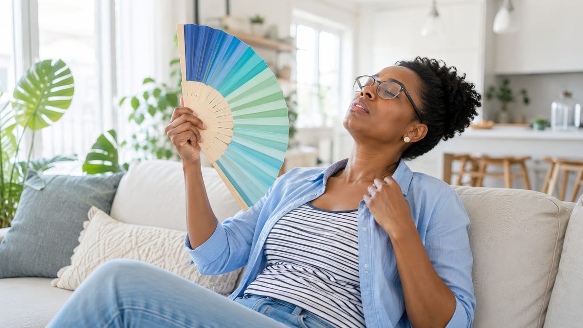 Woman on couch having hot flash fanning herself with a colorful fan.
