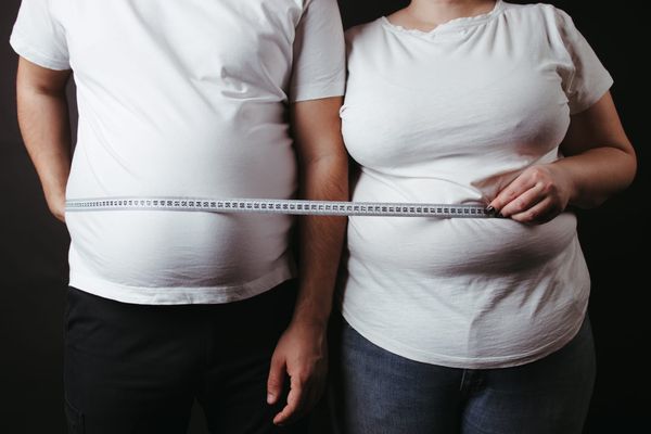 Male and female bodies with high BMI holding tape measure across their midsections
