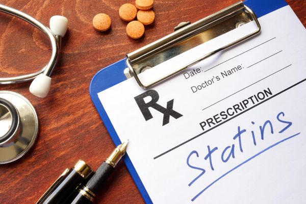 "Statins" written on prescription pad. Pens, pills, and stethoscope in background. 