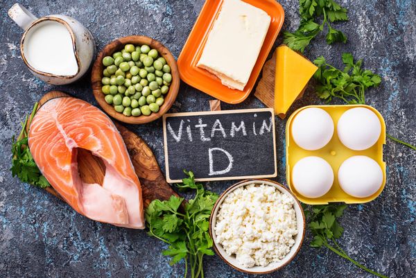 Food around a chalkboard sign that says Vitamin D: salmon, peas, dairy, herbs, cheese, eggs. 