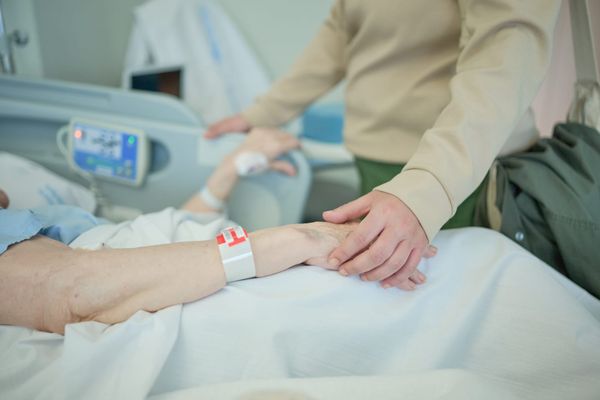 Person holding hand of patient in hospital bed.