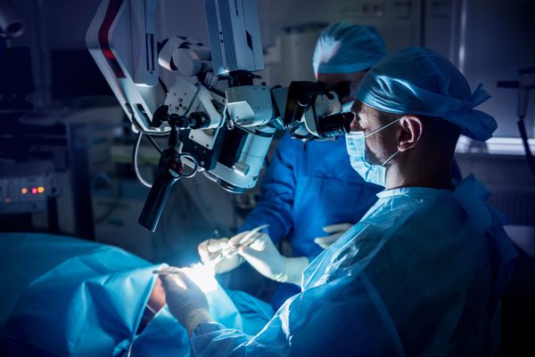 Two doctors perform brain surgery on a patient lying on the operating table. 