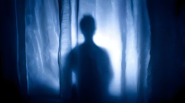Human figure illuminated behind a curtain.