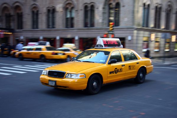 Taxi drives through a metropolitan intersection with other taxis in the background. 