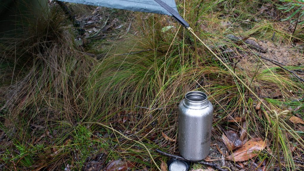 Collecting rainwater from tarp into a drink bottle