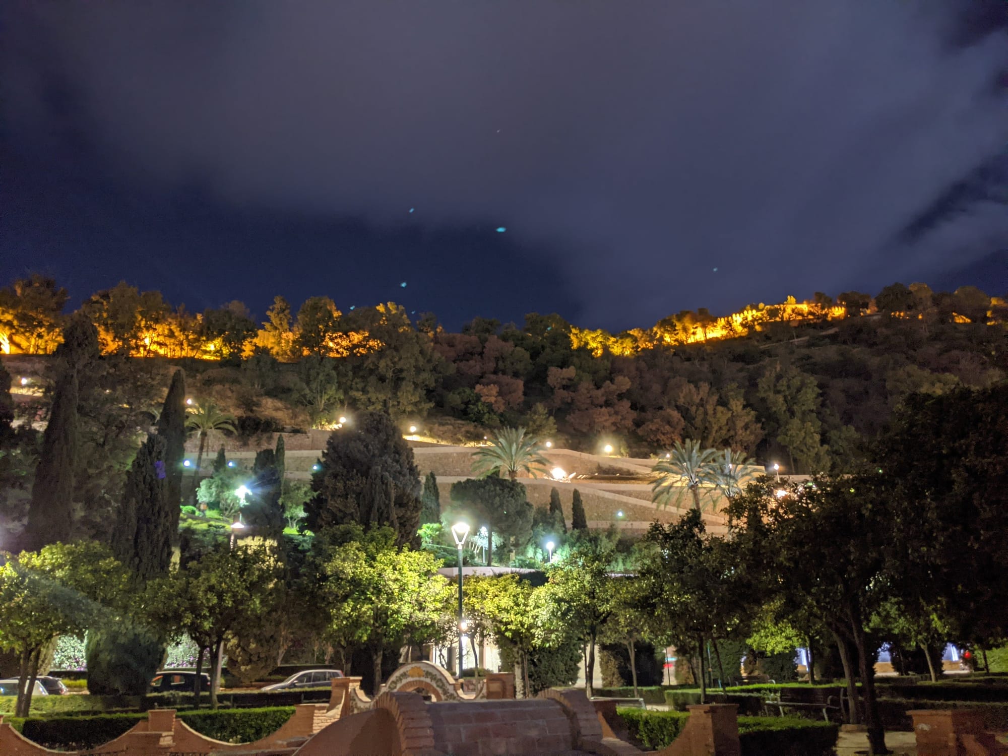 Windy tree lined path leading up to lit castles on a cloudy night