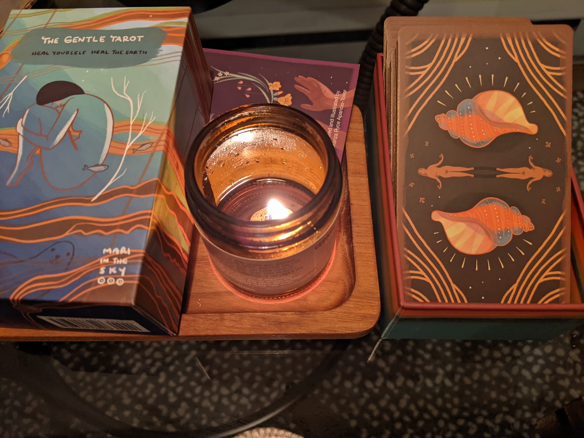 The Gentle Tarot deck by Mari in the sky, a lit candle, and the cards face down pictured left to right