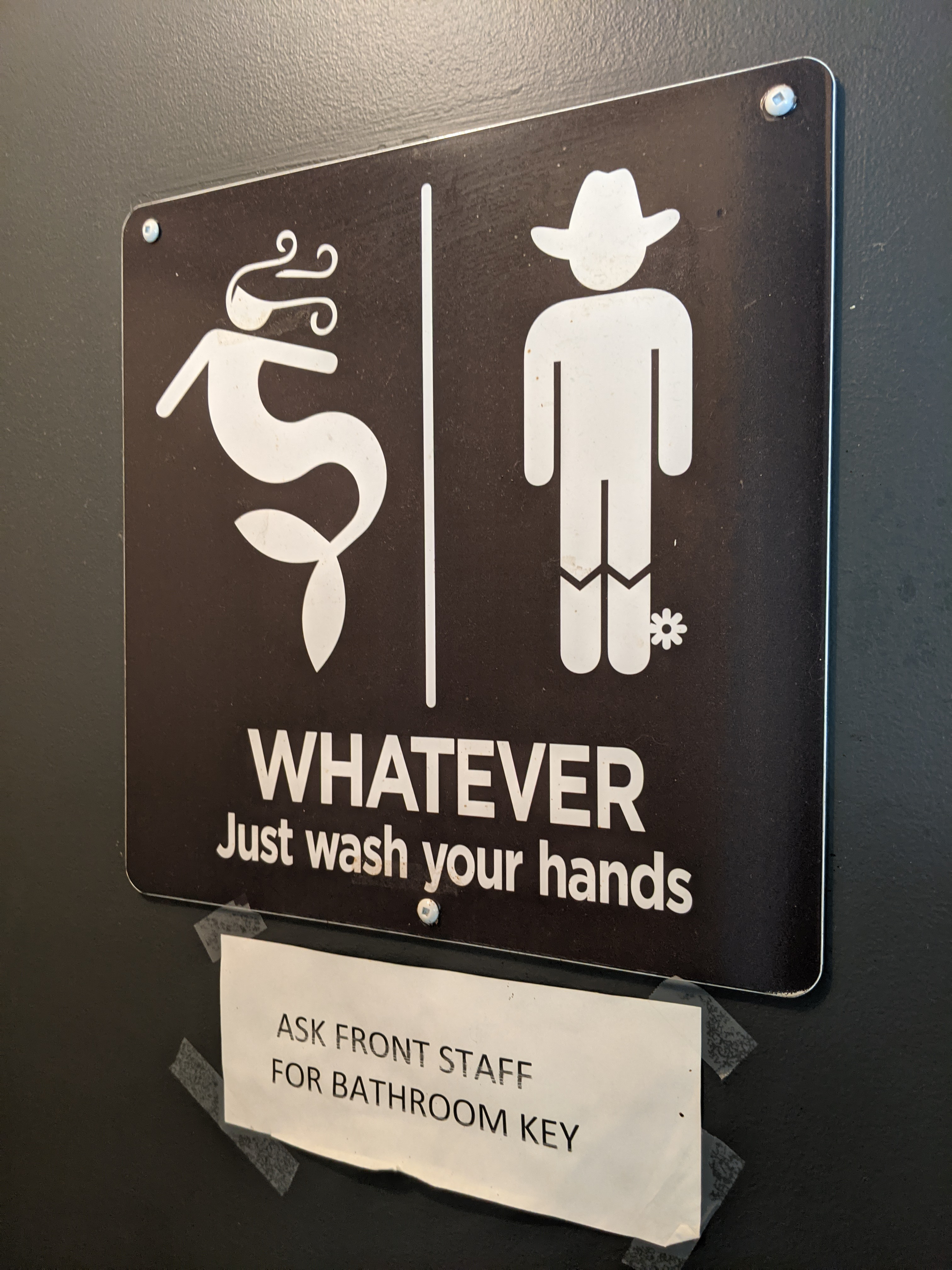 A bathroom door with mermaid and rancher graphics with the text, "WHATEVER Just wash your hands" underneath.