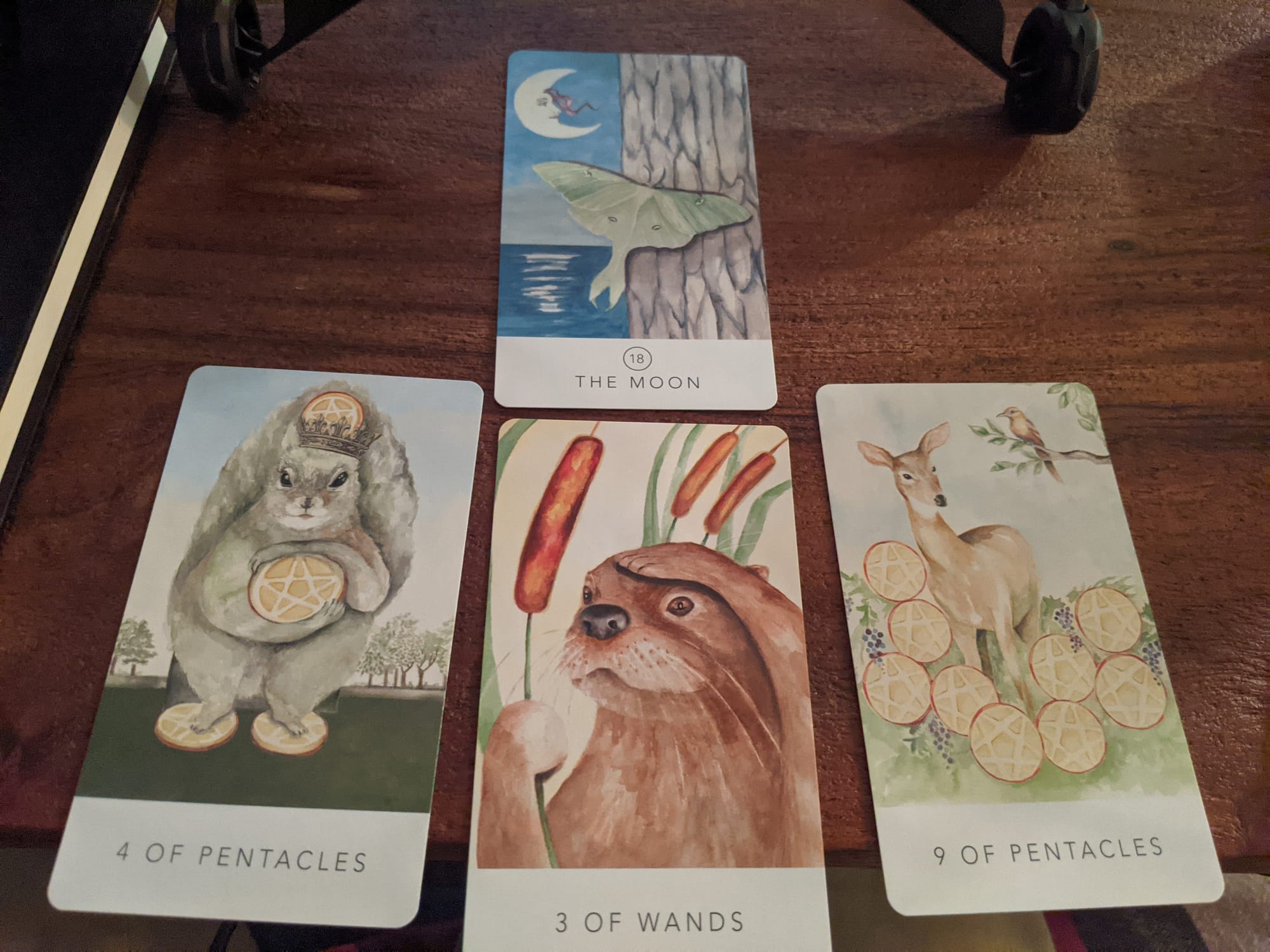 Past: 4 of Pentacles, Present: 3 of Wands, Future: 9 of Pentacles, Back of deck: The Moon, Tarot cards spread on a wooden table, from Black Seed Tarot by Teresa Hutch