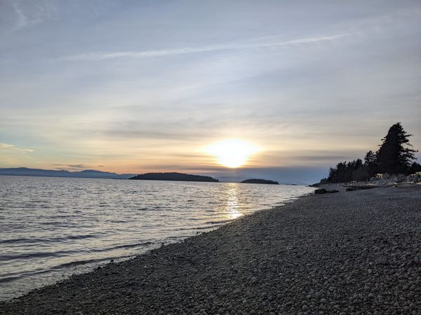 sun sets over mountains at a pebble beach on the west coast