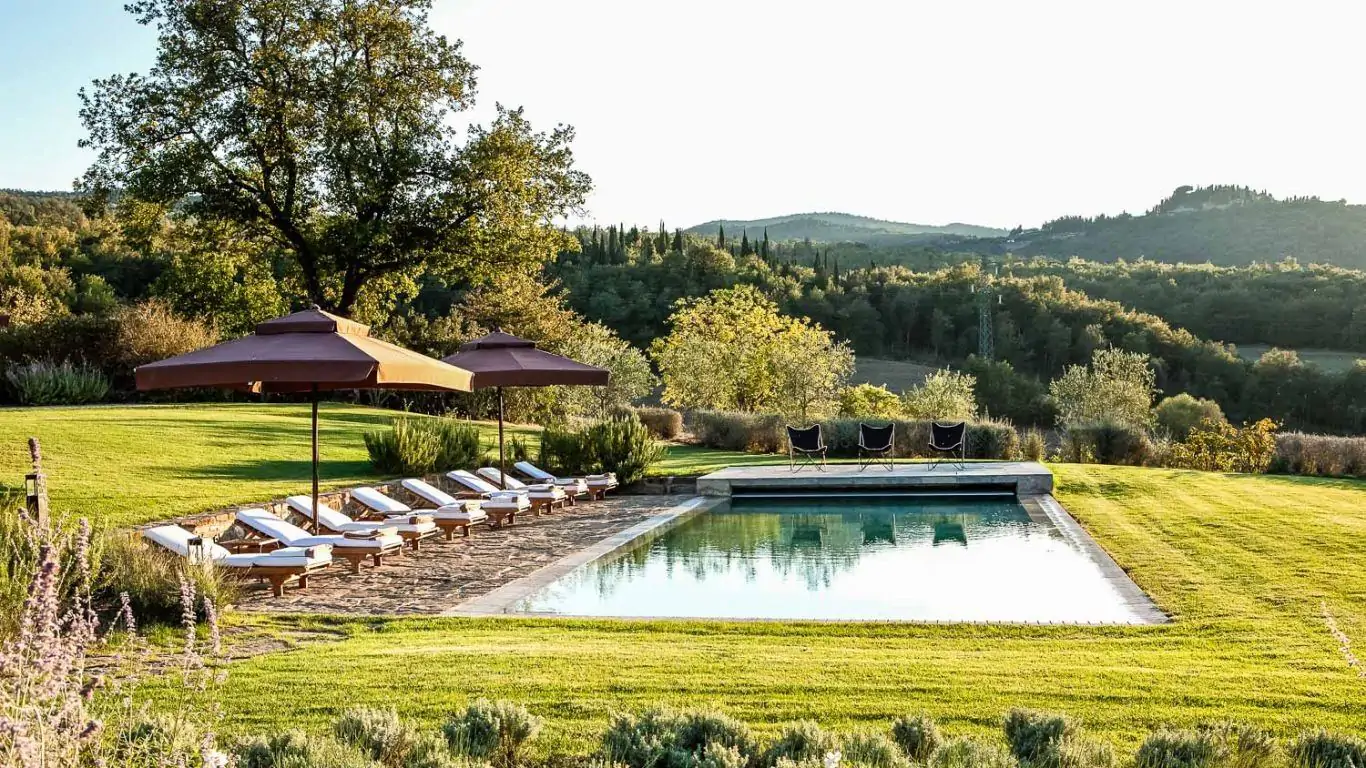 An exquisite view of Villa Gauggiole in Tuscany with a sparkling pool and scenic countryside and verdant hills in the backdrop.