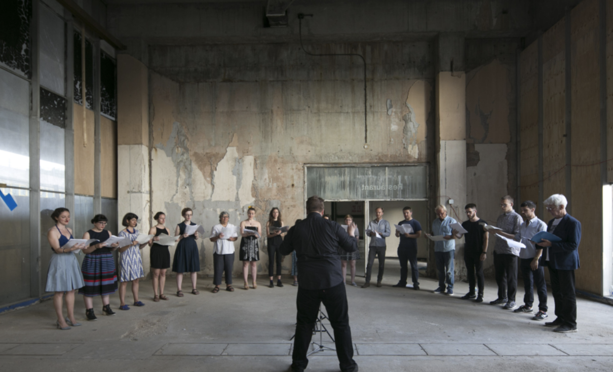 LFA’s choir of around twenty people stands in a semi-circle inside an industrial space and exposed concrete.