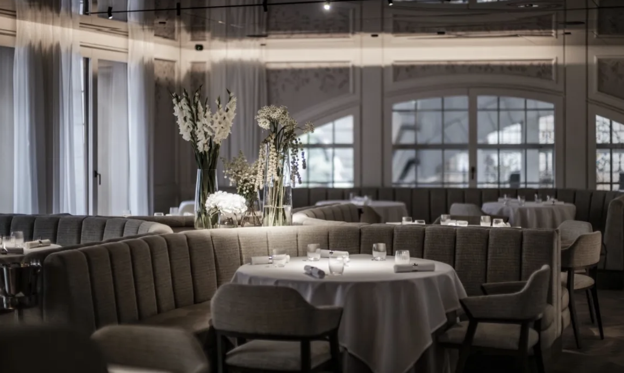 Alex Dilling’s softly lit dining room is adorned with plush grey seating and tables draped in white linens. 