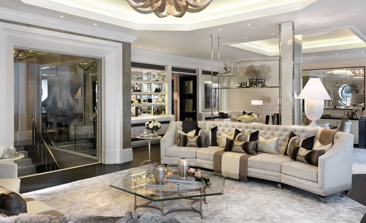  A luxurious living area with a tufted sofa, elegant glass coffee table, and mirrored shelving.&nbsp;