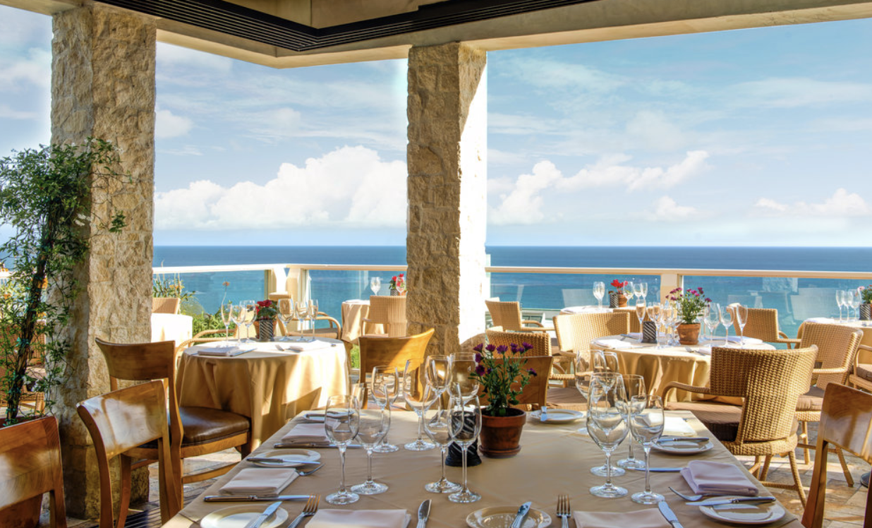 Sunlit balcony dining area overlooking the azure water of the Pacific coastline.&nbsp;
