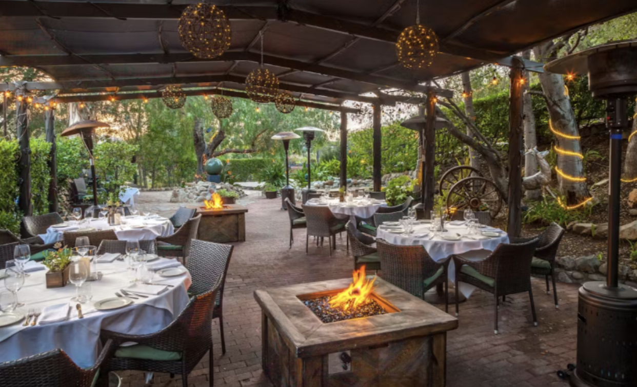 Fire pits, string lights, and lush gardens adorn this elegant outdoor dining patio.