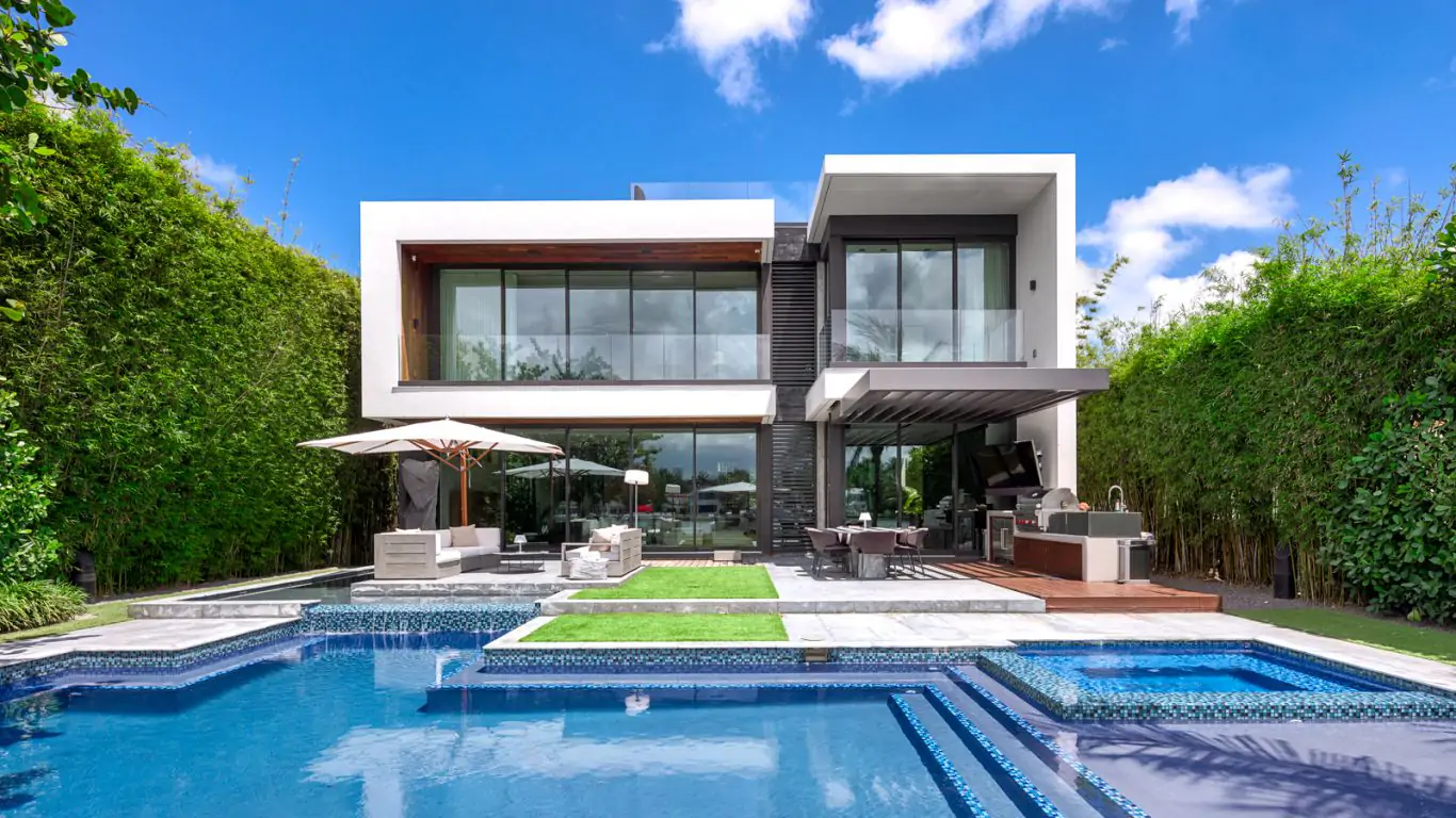 Villa Aria in Miami featuring sleek, modern architecture, spacious pool area, lush greenery, and inviting outdoor lounge spaces.