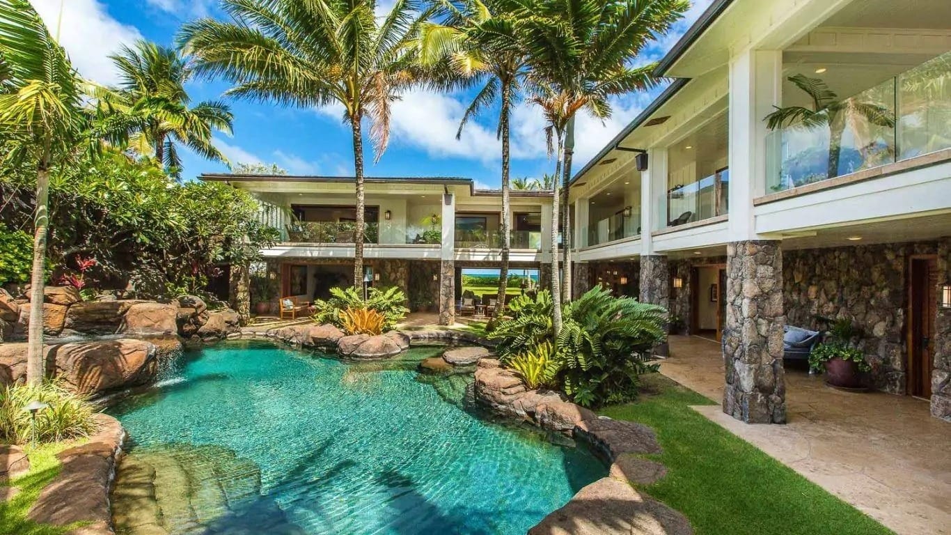 Royal Kailua Estate in Hawaii features a lagoon-style pool, lush tropical landscaping, and elegant stone architecture. A luxury vacation rental near top golf courses in Oahu.&nbsp;