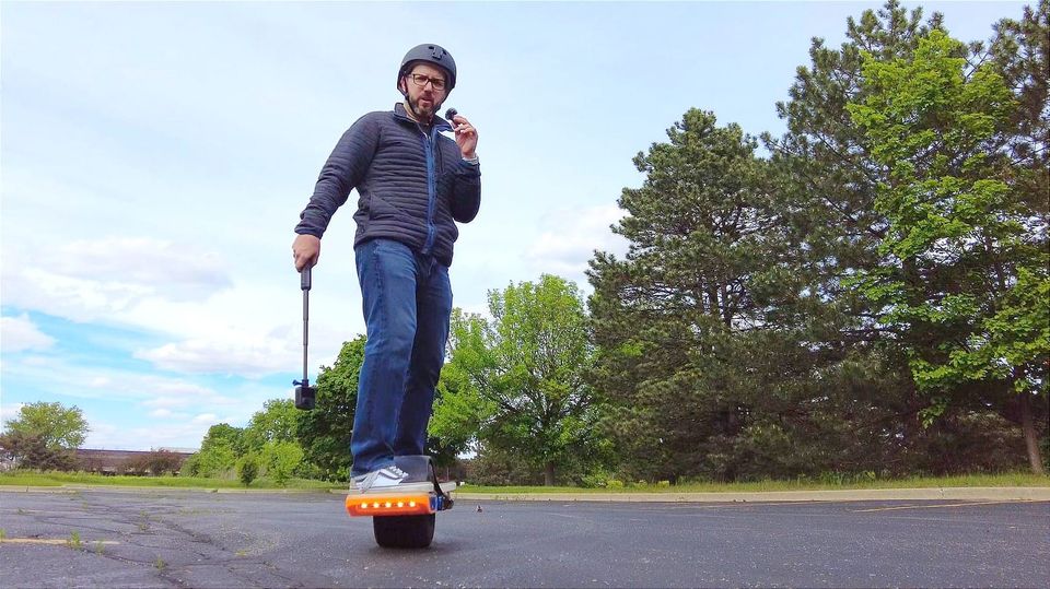 Kevin riding his OneWheel with a 360 camera in one hand an a microphone in the other