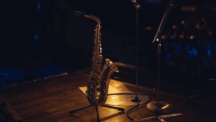 A saxophone stands upright in a silver saxophone stand on a wooden stage floor before the jazz concert begins.